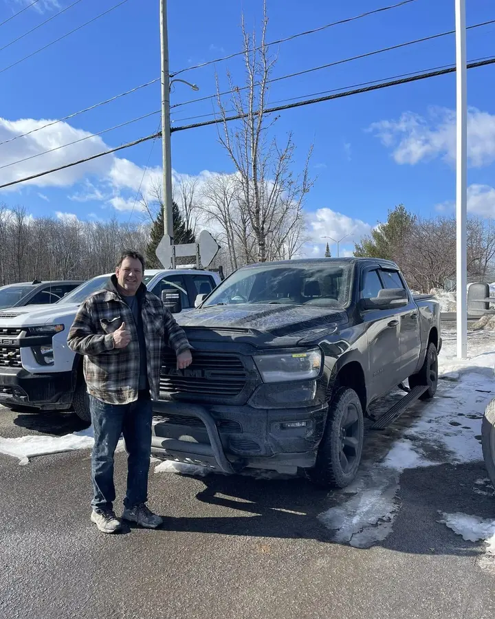 Client, pouce levé, devant son Ram 1500 noir vendu à En Ligne Autos